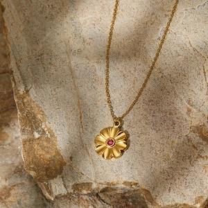 Artistic close-up of gold flower pendant necklace with pink gemstone on light rock texture