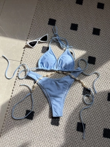 Light blue bikini set with shell chain detail laid on beige rug with sunglasses