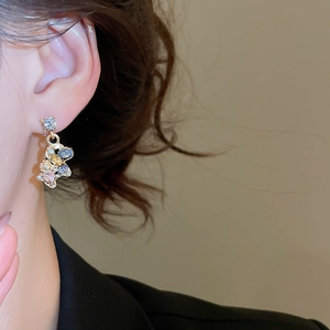 Macro view of gold stud earring featuring a colorful rhinestone-encrusted bear pendant