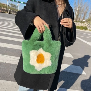 Green plush tote bag with fried egg pattern and metal chain strap worn on black coat