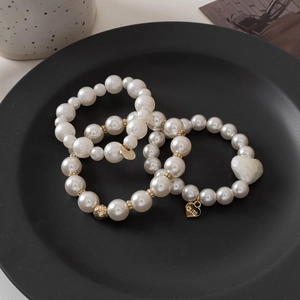Detailed view of three pearl bracelets with gold DREAM and CUTE charms on a tray