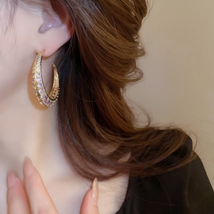 Detail of elegant gold-plated C-shaped earrings with purple zircon on a model