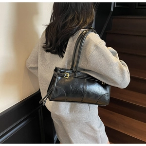 Detail view of stylish black leather shoulder bag with gold buckle on model shoulder