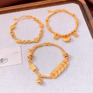Macro detail of 24K gold plated bracelets featuring classic coins and floral charms