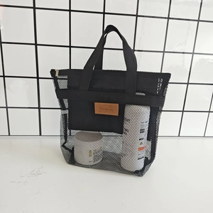 Dettaglio della borsa a rete nera con etichetta in pelle marrone su tavolo bianco
