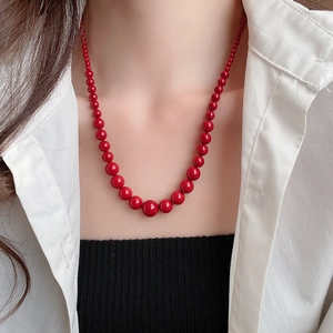 Détail d'un collier de perles rouges luxueux porté par un mannequin sur une chemise blanche