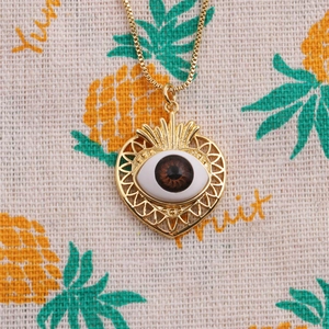 Gros plan détaillé du collier cœur doré avec incrustation d'œil réaliste et chaîne fine