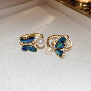 Detail view of butterfly rings with freshwater pearls and blue shell wings on gold plating