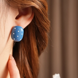 Dettaglio orecchino ovale blu a pois bianchi indossato da una modella per look di moda