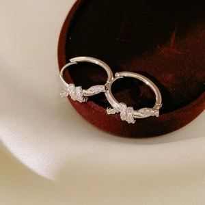 Macro detail of silver knot hoop earrings with micro-inlaid zircons on red velvet
