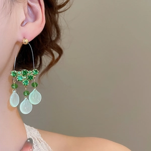Detail of green zircon and teardrop shell tassel earrings worn on a female model
