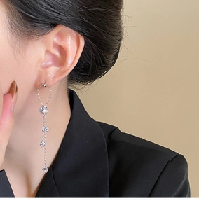Detail view of long silver tassel earrings with zircons worn by a model in a black blazer