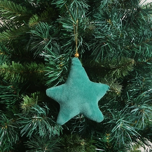 Close-up of a green velvet star-shaped Christmas ornament hanging on pine branches