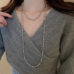 Détail d'un long collier à billes argentées superposé sur un pull gris au style moderne