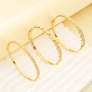 Detailed view of three gold-plated heart-shaped bangles with crystals on white wavy texture