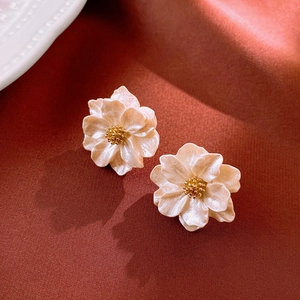 Macro shot of 3D cream white floral stud earrings with pearlescent petals and gold centers