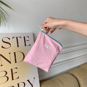 Pink nylon pouch with blue zipper and gold hook held in hand against home background