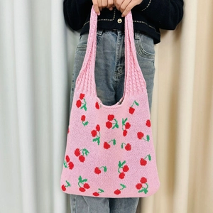 Detail of pink knitted tote bag with cherry patterns and soft yarn texture