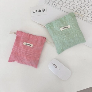 Detail of pink and light green pleated drawstring storage pouches on a clean white desk