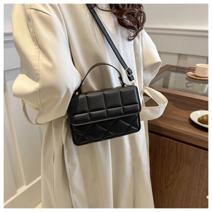 Detail of a black quilted shoulder bag with top handle and adjustable strap on a model