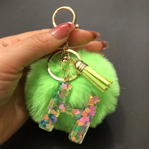 Detail view of resin letter H keychain with green pompom and colorful heart sequins