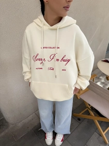 Λεπτομέρεια από κρεμ oversized φούτερ με κόκκινη στάμπα στο στήθος και βαμβακερή υφή