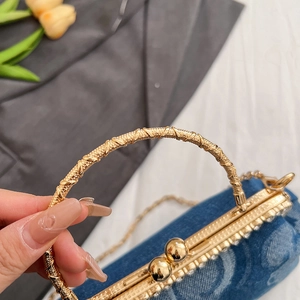 Close-up of blue denim handbag featuring a gold woven handle and pearl chain strap