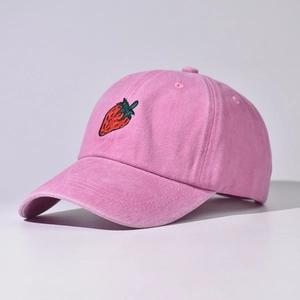 Dettaglio del ricamo a fragola sul berretto da baseball in cotone lavato rosa e consistenza
