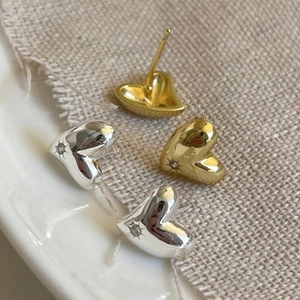 Close-up of gold and silver heart stud earrings with starburst zircon on a linen surface