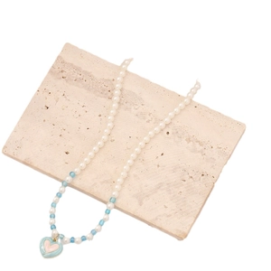 Colorful pearl necklace with blue heart pendant displayed on a minimalist stone plate