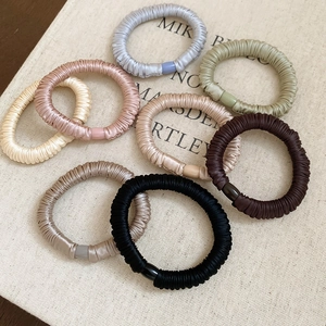 Close-up of silk elastic hair scrunchies in Morandi colors on a textured book surface