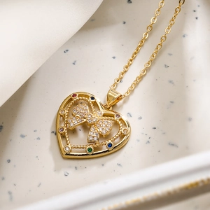 Collana a cuore dorata con fiocco di zirconi e gemme colorate su sfondo bianco
