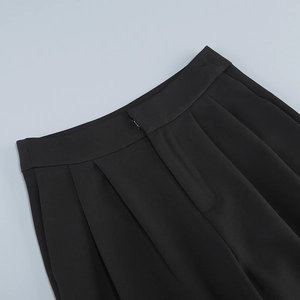 Detailed view of high-waist double pleats and invisible fasteners on black suit trousers