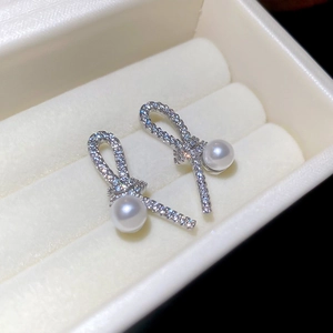 Macro shot of silver knot earrings with pavé crystals and white hanging pearls in a box