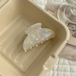 Detailed view of pearlescent white hair claw clip with silver flower accents on soft fabric