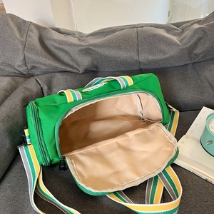 Green cylindrical kids dance duffel bag with striped straps on a gray sofa