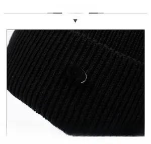 Close-up of black knit beanie texture and oval metal emblem with enamel inlay detail