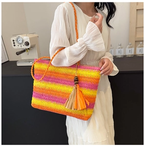 Straw tote bag with orange-pink gradient stripes and wooden bead tassel worn on shoulder