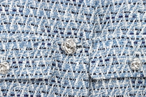 Macro view of blue and white tweed fabric texture with decorative silver metal knot button