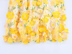 Détail de la broderie florale 3D jaune sur tissu mesh pour une robe de soirée élégante