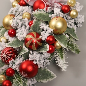 Close-up of red and gold Christmas ball ornaments with frosted leaves on a hanging wreath