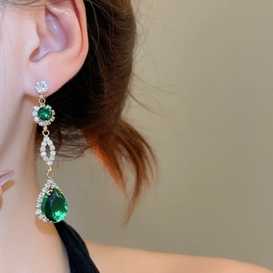 Close-up of dangling drop earrings featuring green pear-cut stones and crystal pave