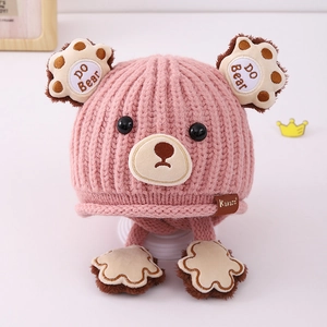 Detail of pink knitted bear hat for kids with earflaps and cute paw print straps