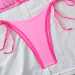 Detail of shocking pink bikini bottoms with side-tie design on white cotton fabric