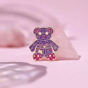 Macro detail of cartoon purple bear enamel pin with heart and star patterns