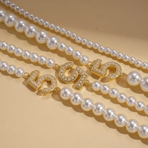 Detail of faux pearl layered necklace with gold number 5 charms and intricate inlay
