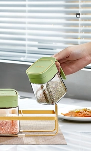 Ergonomic avocado green spice jar with gold trim and transparent glass body on a gold rack