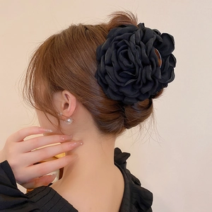 Close-up of a large black fabric rose hair claw clip styled on a low bun hair look