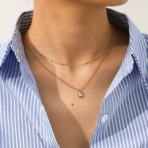 Detail of double-layer gold stainless steel necklace with rectangular pendant on a model