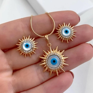 Detail der handgehaltenen Gold-Sonnenkette und der blauen Augen-Ohrringe mit Kristallen